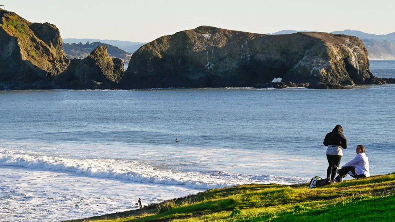 People on a green bluff overlooking the waves of the Pacific Ocean.