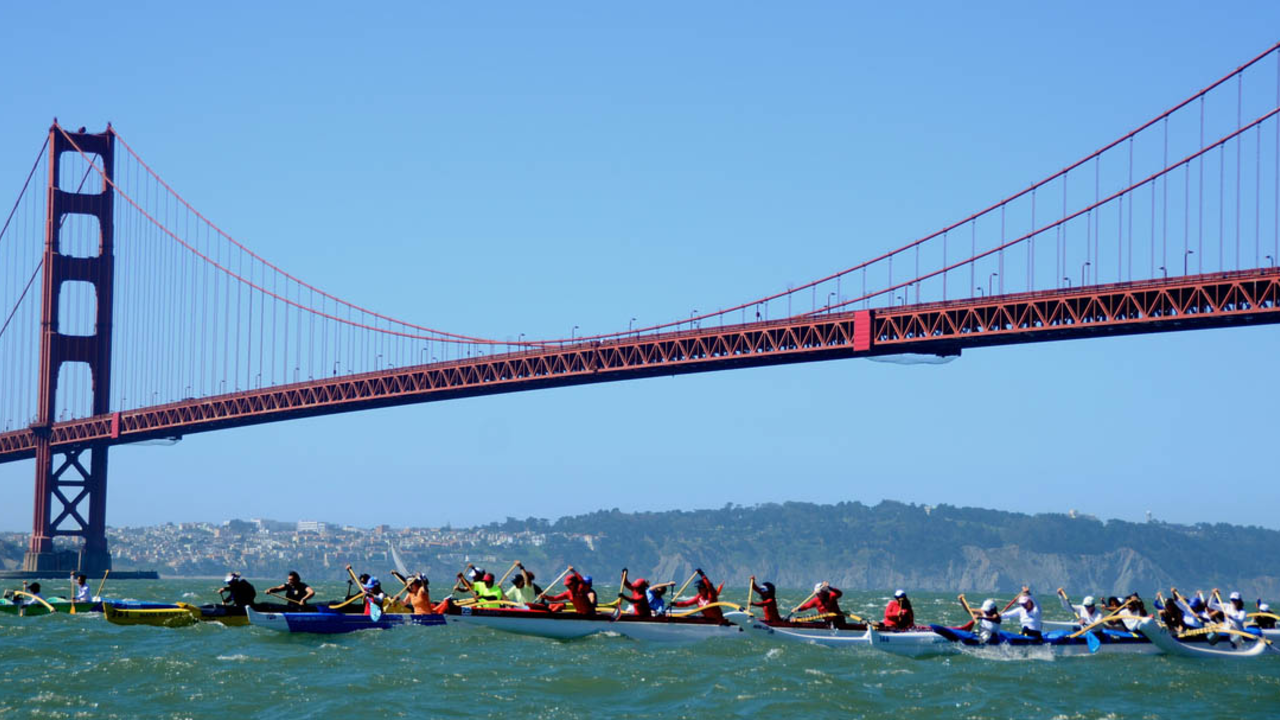 Outrigger canoes paddle under the Golden Gate Bridge.