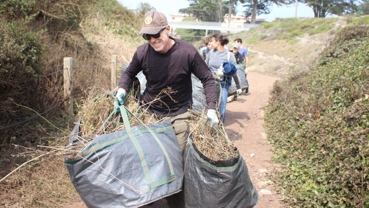 PRBL_180823_YP-(7)_2x1.jpg A volunteer carries large bags of vegetation while walking on a trail