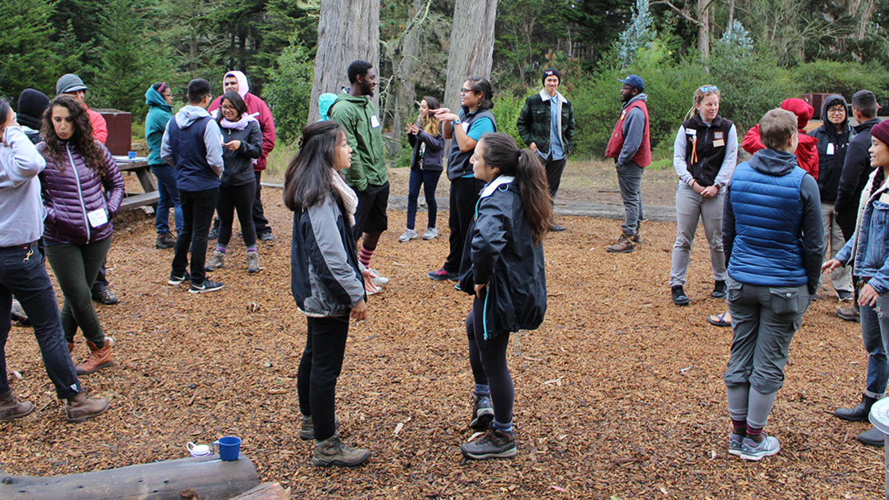 A large group of people stand outside in pairs and speak to their partners during a leadership training 
