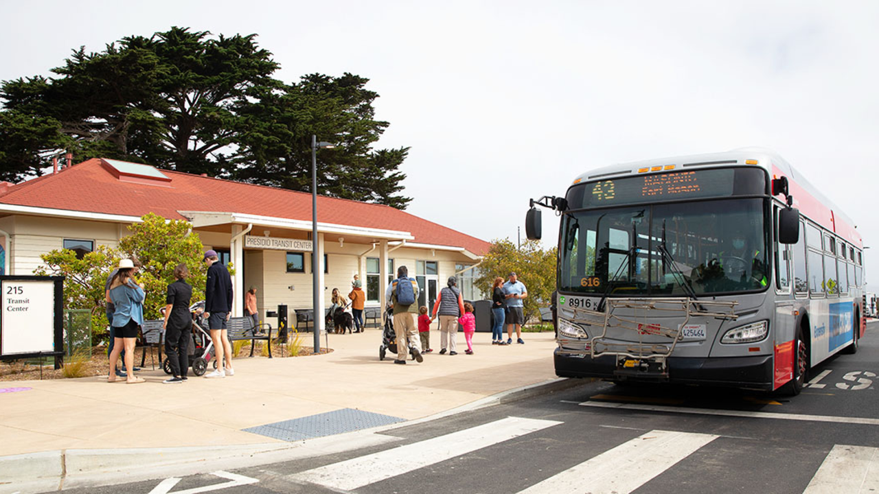 A red and gray San Francisco Muni bus parked at a station in the Presidio