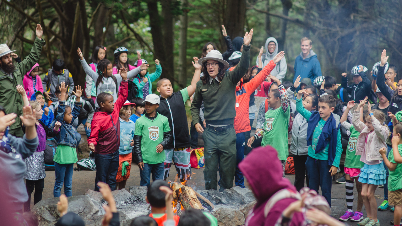 A National Park Service Ranger leads a large group of smiling children in an interactive story