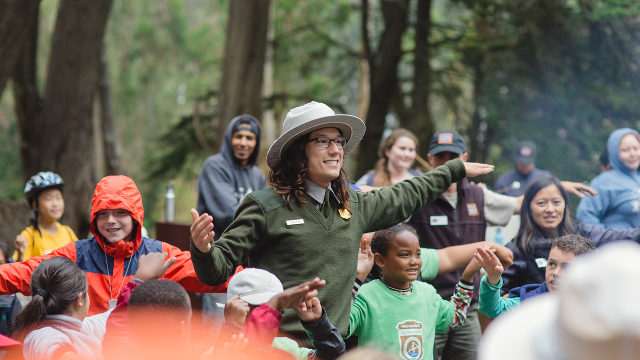A National Park Service Ranger leads a large group of smiling children in an interactive story