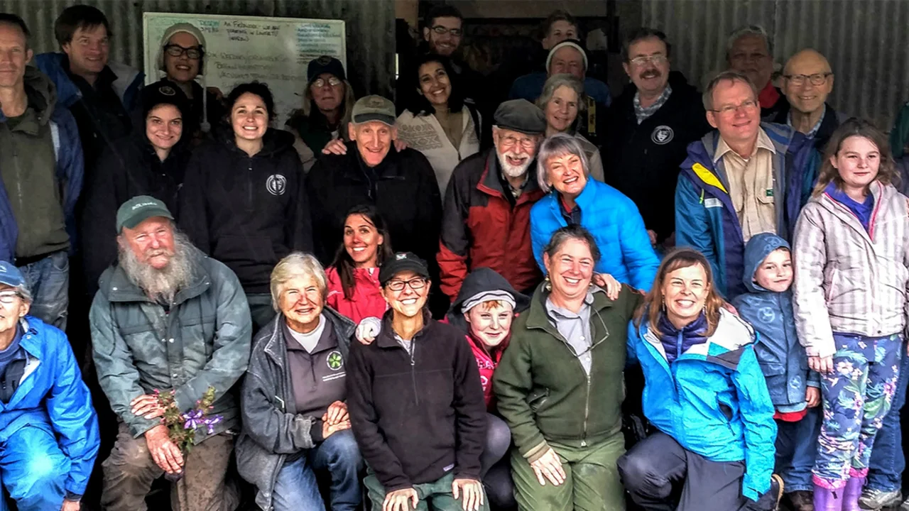 A large group smiles while posing for a photo in front of a metal barn.