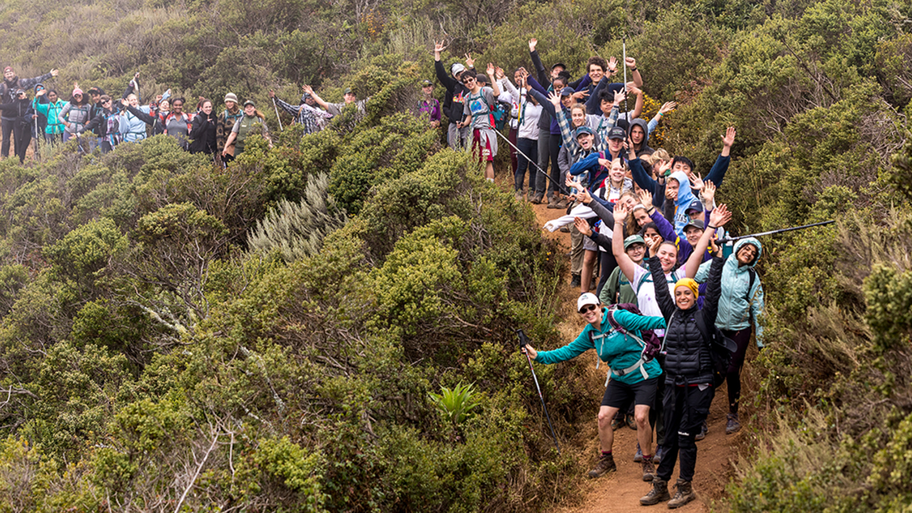 Ranger-led hike people standing on a trail waving at the camera with bushes in landscape