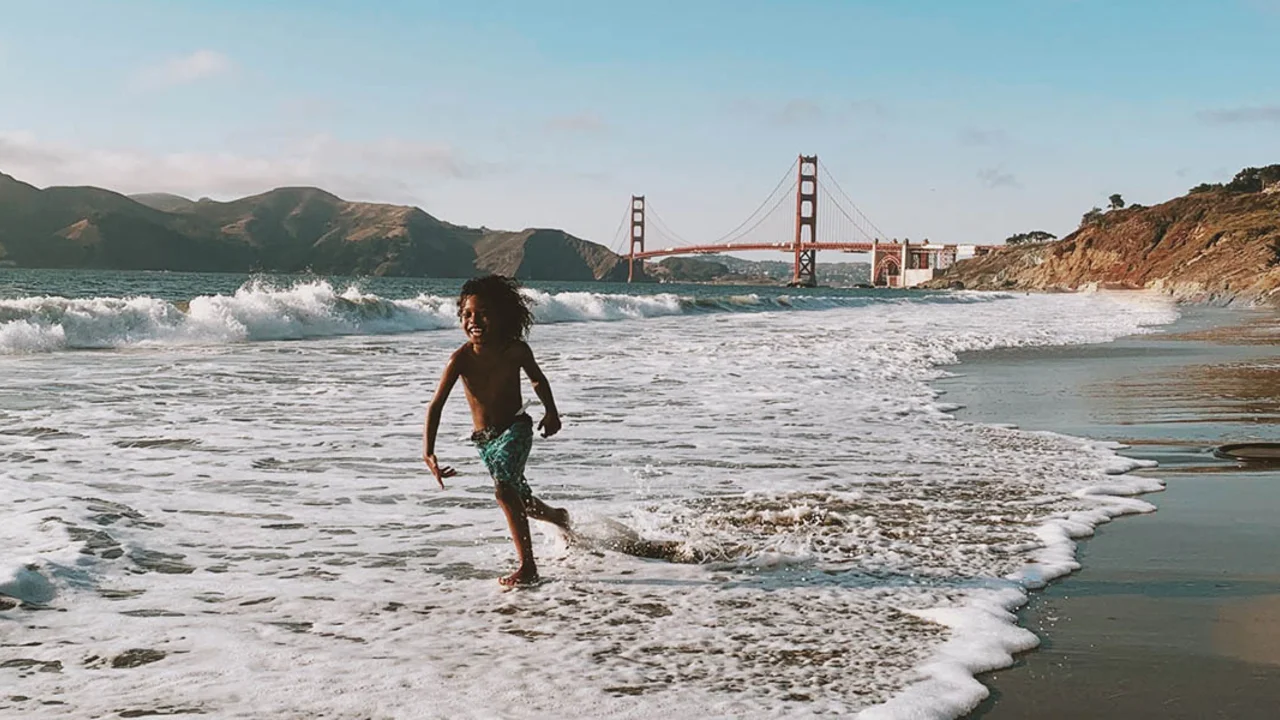 Child plays in the waves with Golden Gate Bridge in background.
