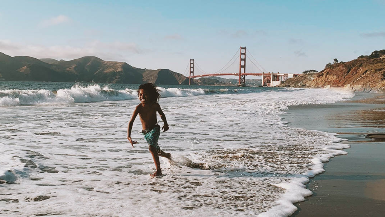 Child plays in the waves with Golden Gate Bridge in background.