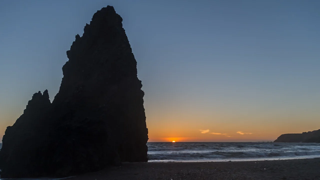 Sunset on the horizon with mitten-shaped rock formation on left.