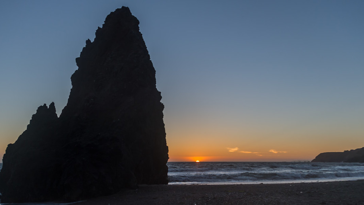 Sunset on the horizon with mitten-shaped rock formation on left.