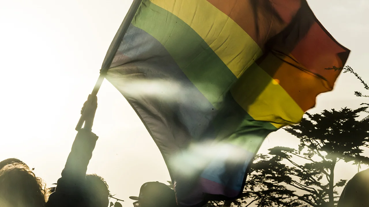 A sunset photo of the rainbow pride flag flying in the parks.
