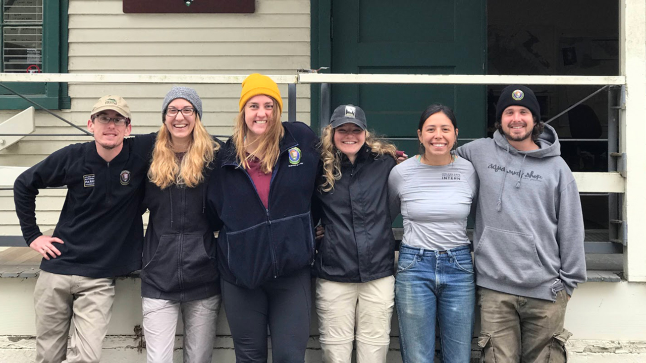 A group of interns pose together outside of a building while smiling at the camera