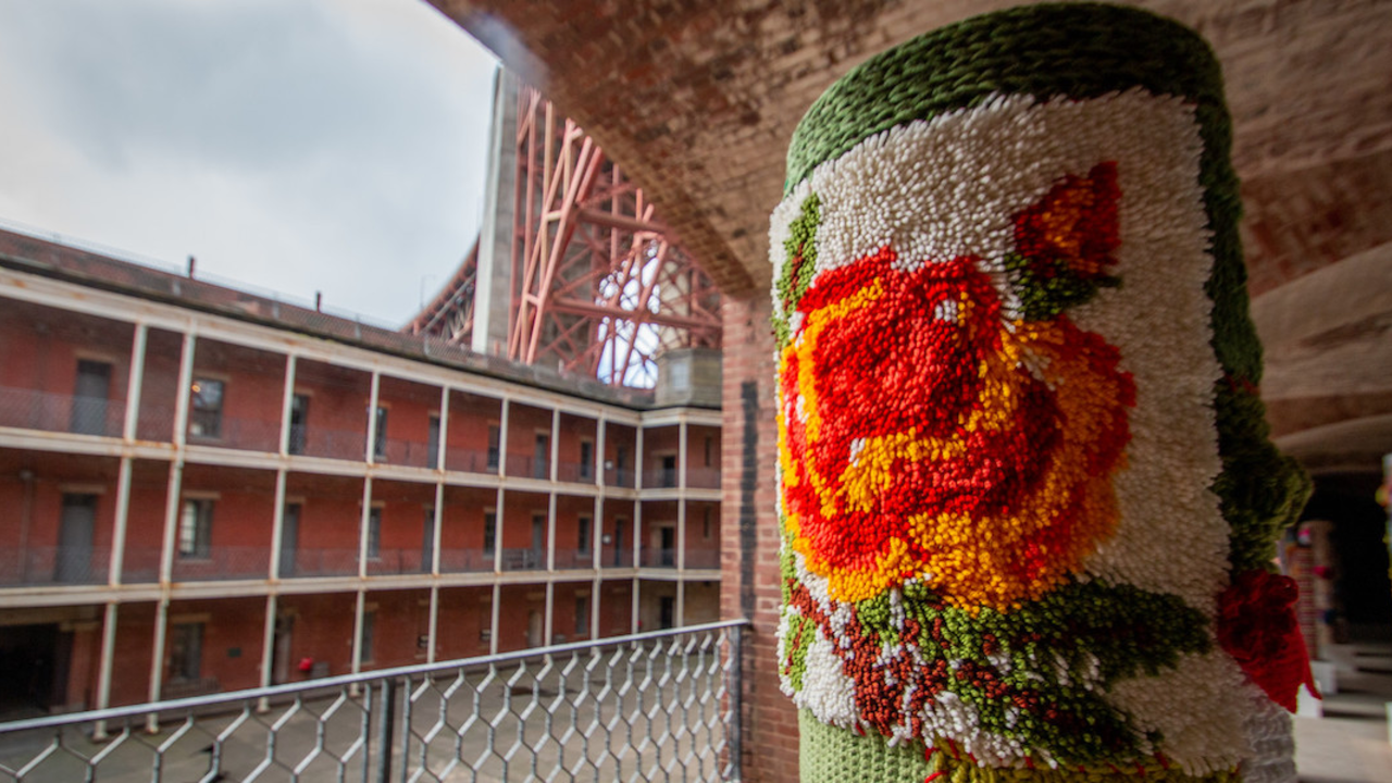 Pole covered in yarn with Fort Point and Golden Gate Bridge in background.