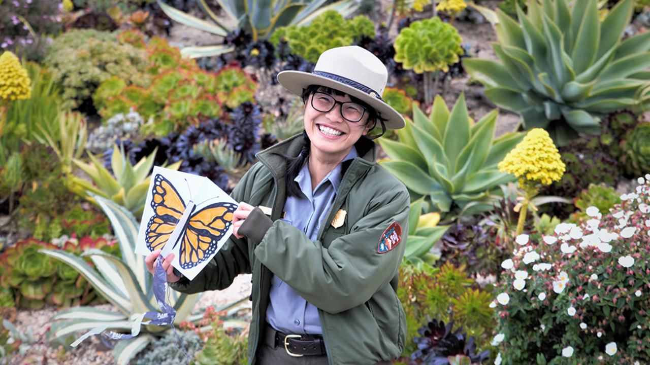 Ranger Rebecca Au poses with a butterfly drawing in a flower field.