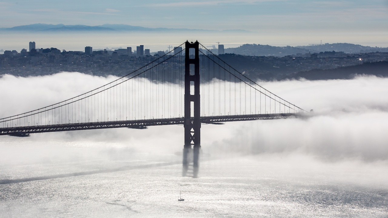 Golden Gate bridge in a layer of fog with a view of San Francisco behind it. 