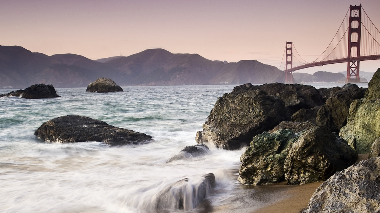 Waves crashing over rocks at Marshall's Beach with Golden Gate Bridge in the background.