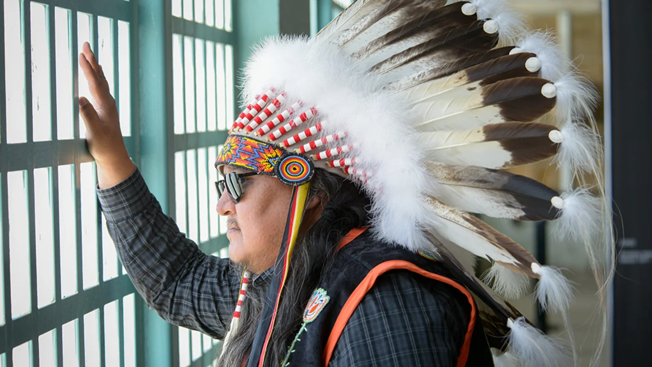Man in native american headress looking out window of bars