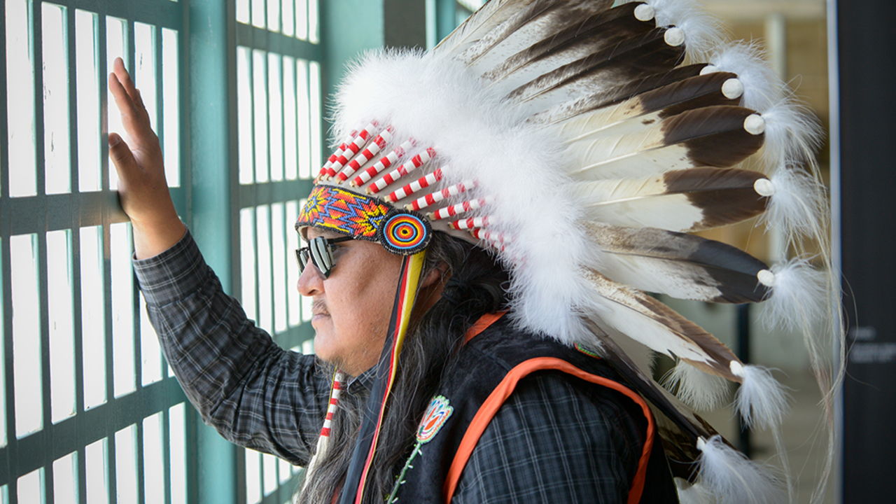 ALCA_20191120_RCW_0050.jpg Man in native american headress looking out window of bars