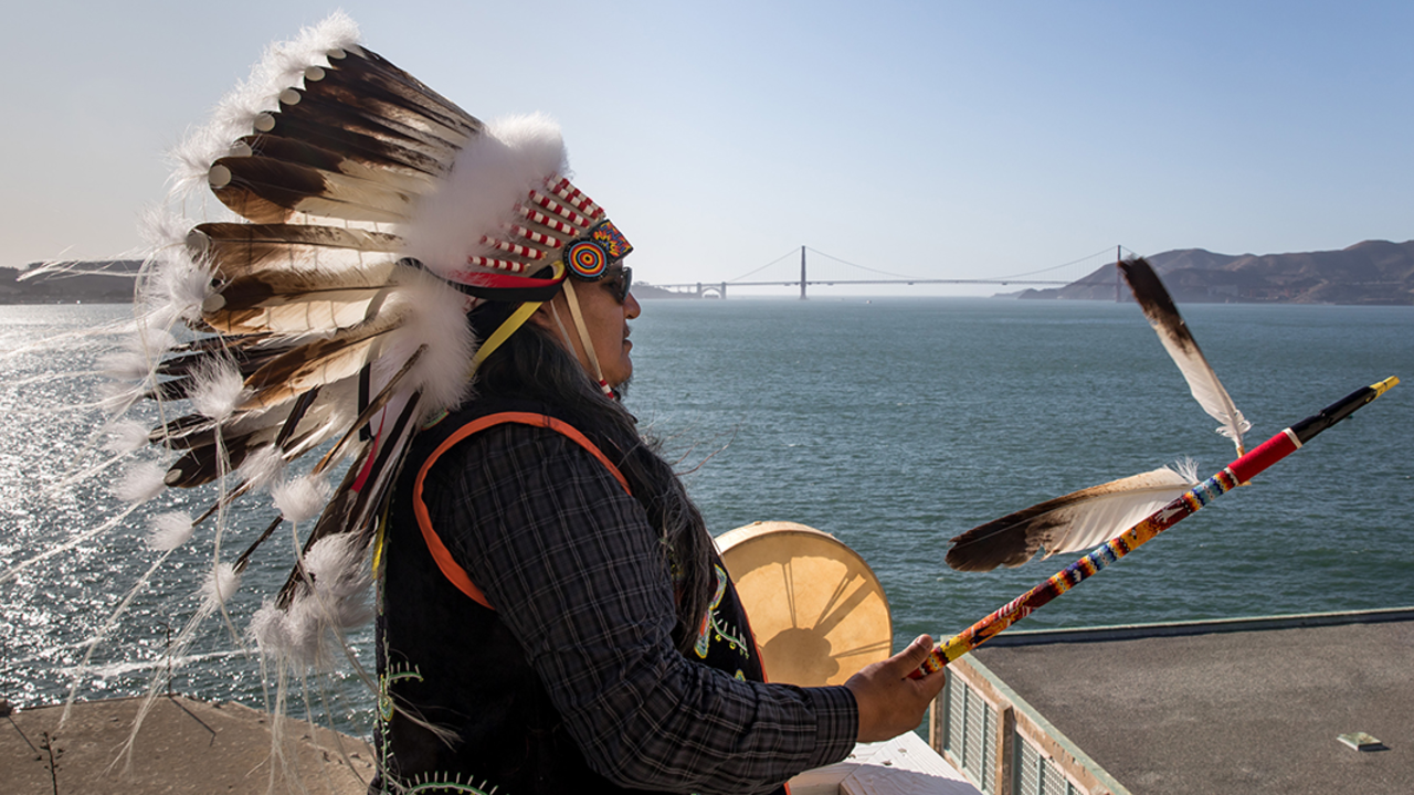 Profile of man with golden gate bridge in background.  The tide is going out and the sky is blue.