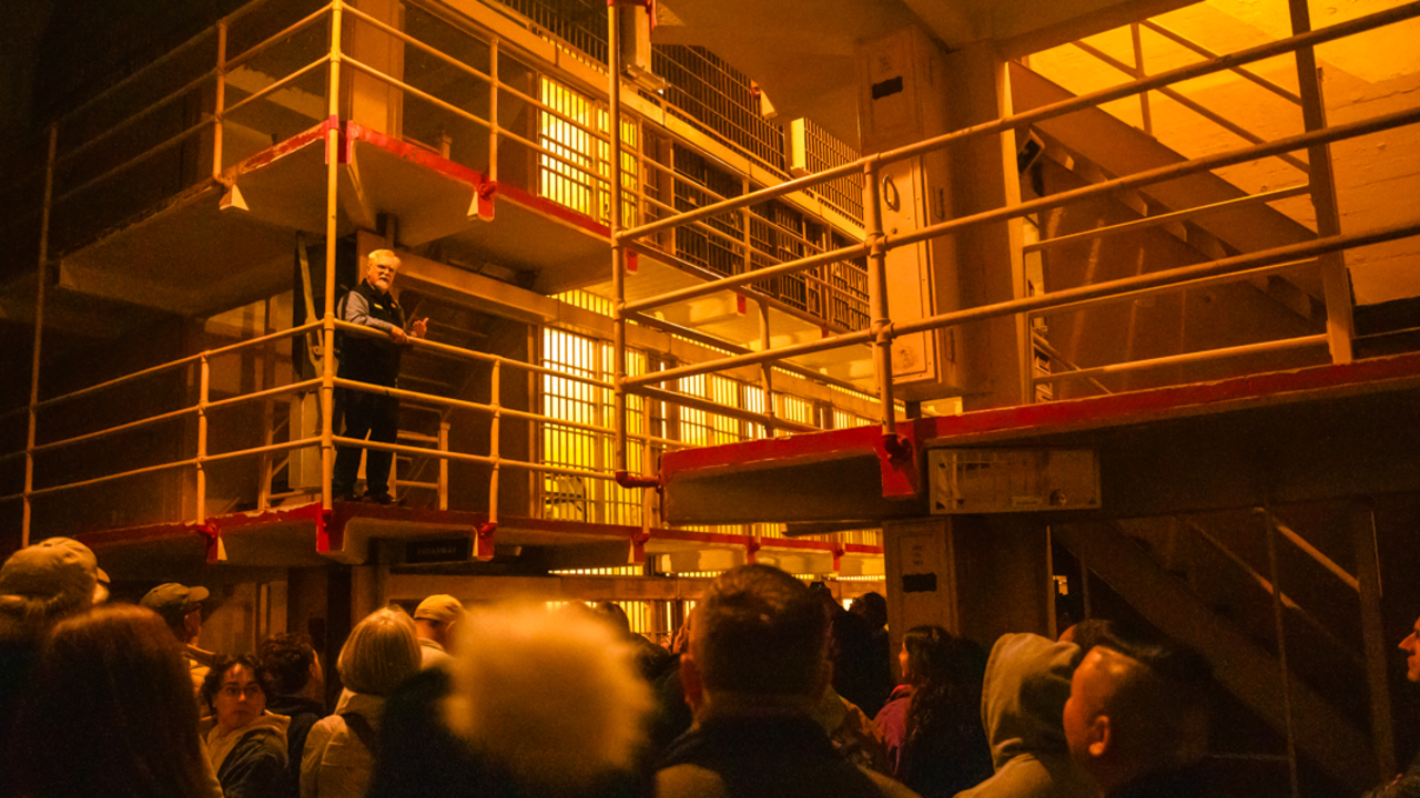 Alcatraz Night Tour An Alcatraz tour-guide demonstrates the prison cell door mechanisms to a crowd under dim light during the night tour