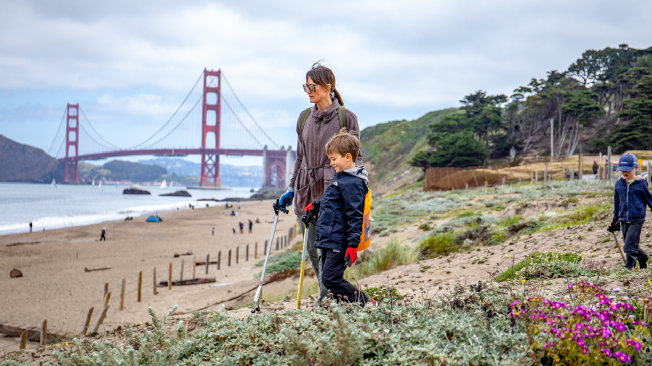 A family looks out to sea at a Baker Beach cleanup event, golden gate bridge in the background.