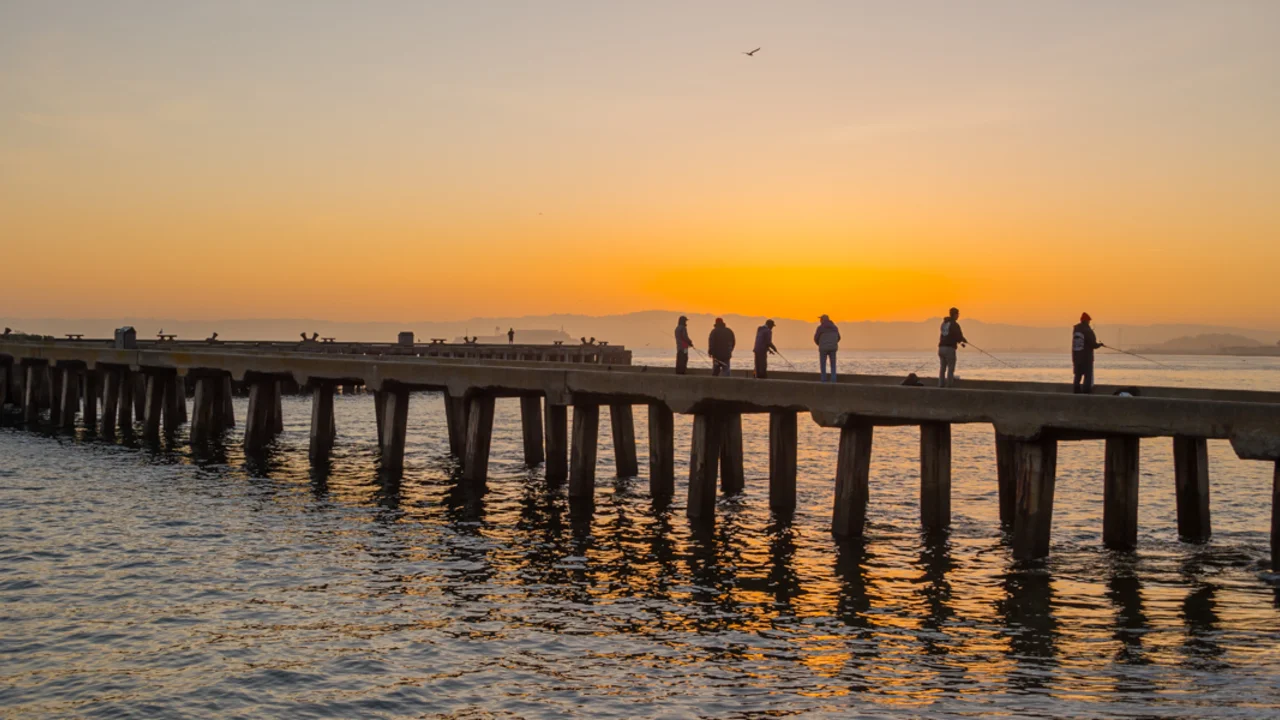 The sun rises over the bay waters, visitors are seen fishing off of the pier at Crissy Field.