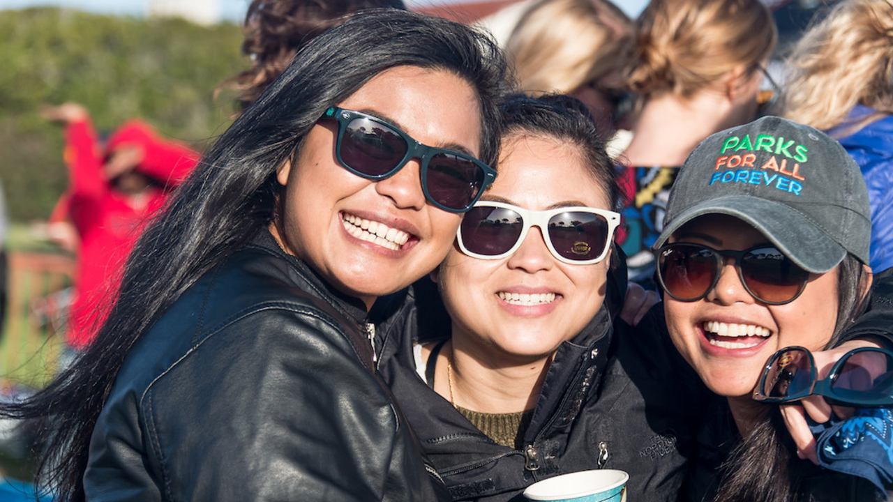 Three woman wearing sunglasses smile for photo.