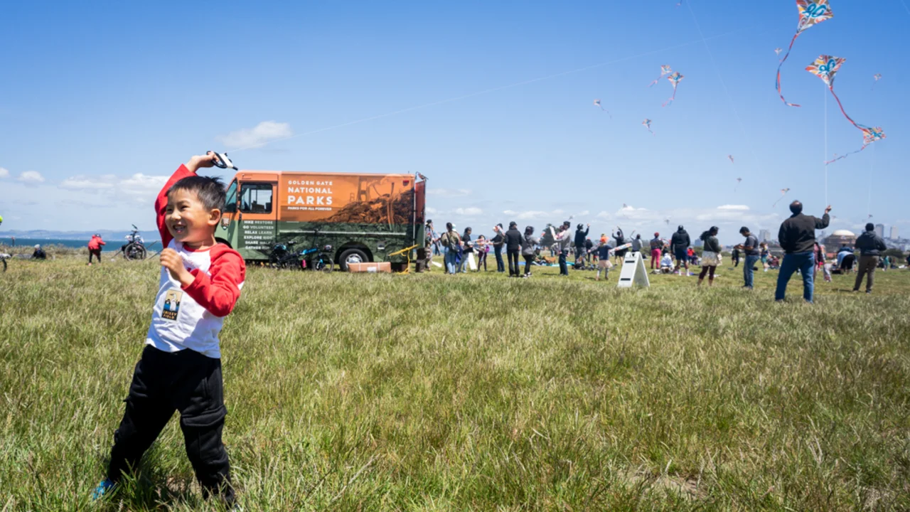 A child smiles flying a kite alongside the Roving Ranger at Crissy Field.