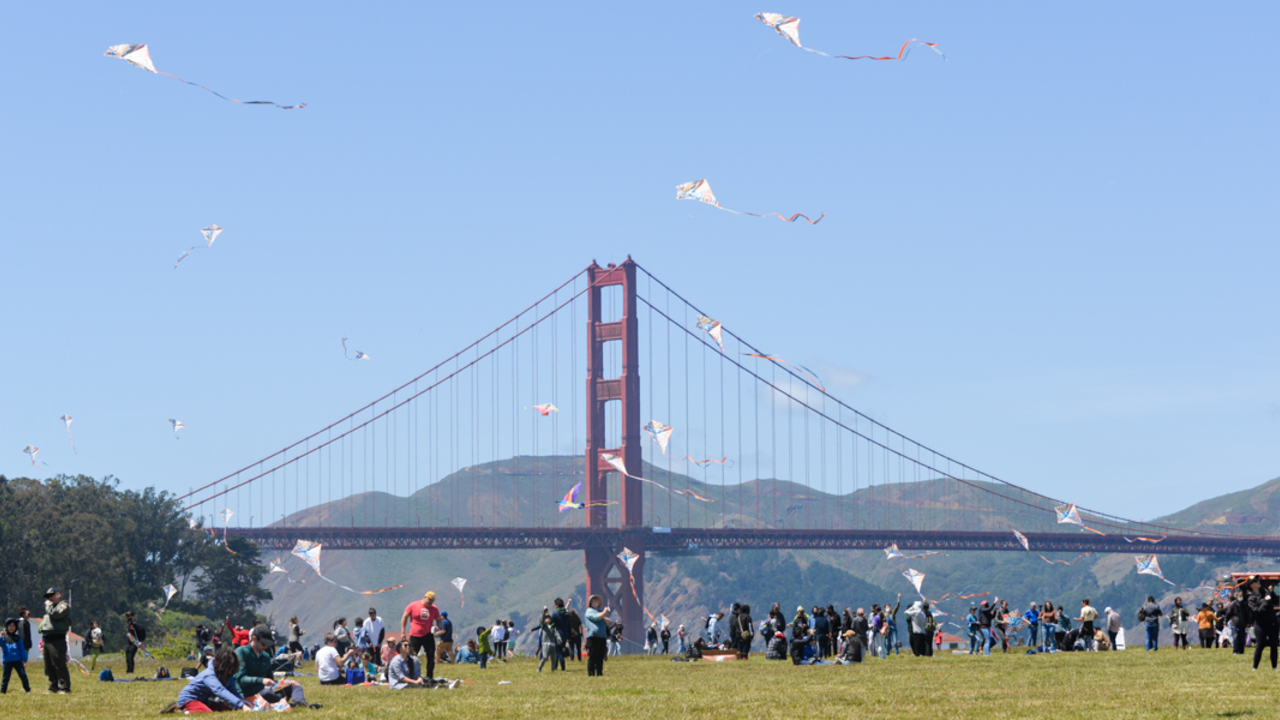 A crowd flies kites on Crissy Field A crowd amasses at Crissy Field Kite Day, flying their kites with the Golden Gate Bridge in the background.