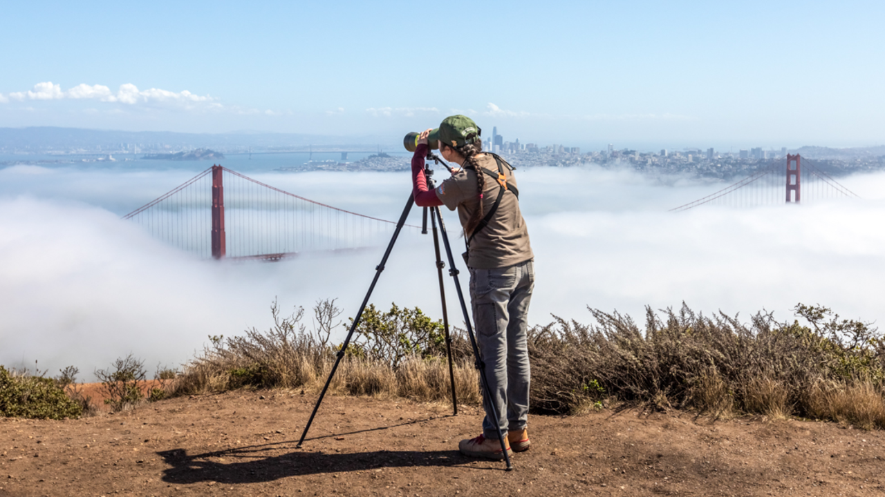 A woman peers through a birding telescope looking over the golden gate bridge and san francisco bay