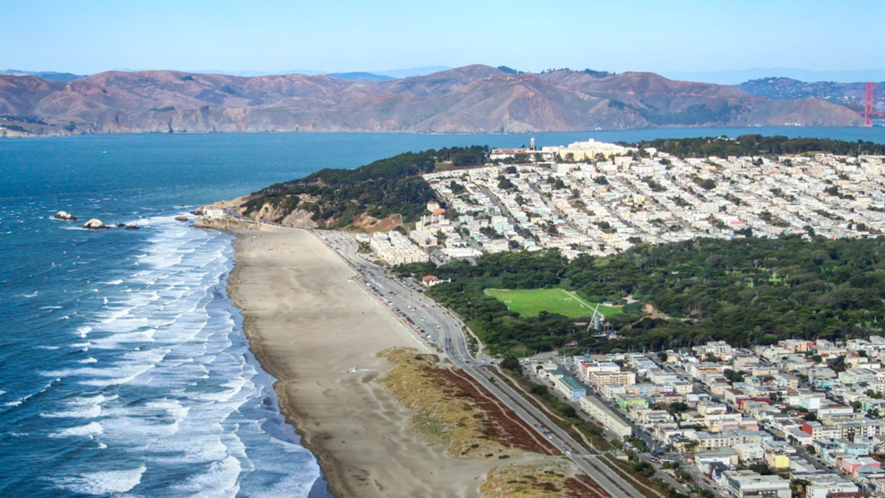 Aerial view of Ocean Beach showing waves lapping against the shore before San Francisco, along with the Golden Gate and Marin Headlands in the background.