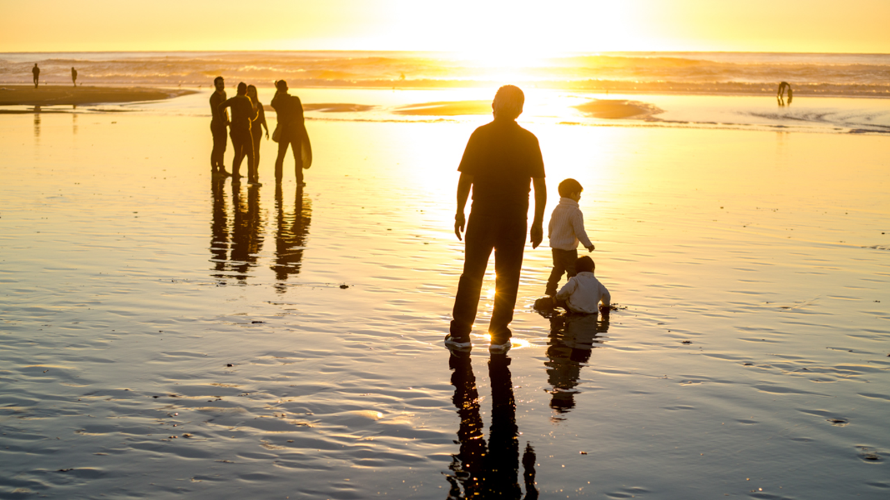 Visitors and families bask in a golden sunset where the water meets the sands of Ocean Beach.