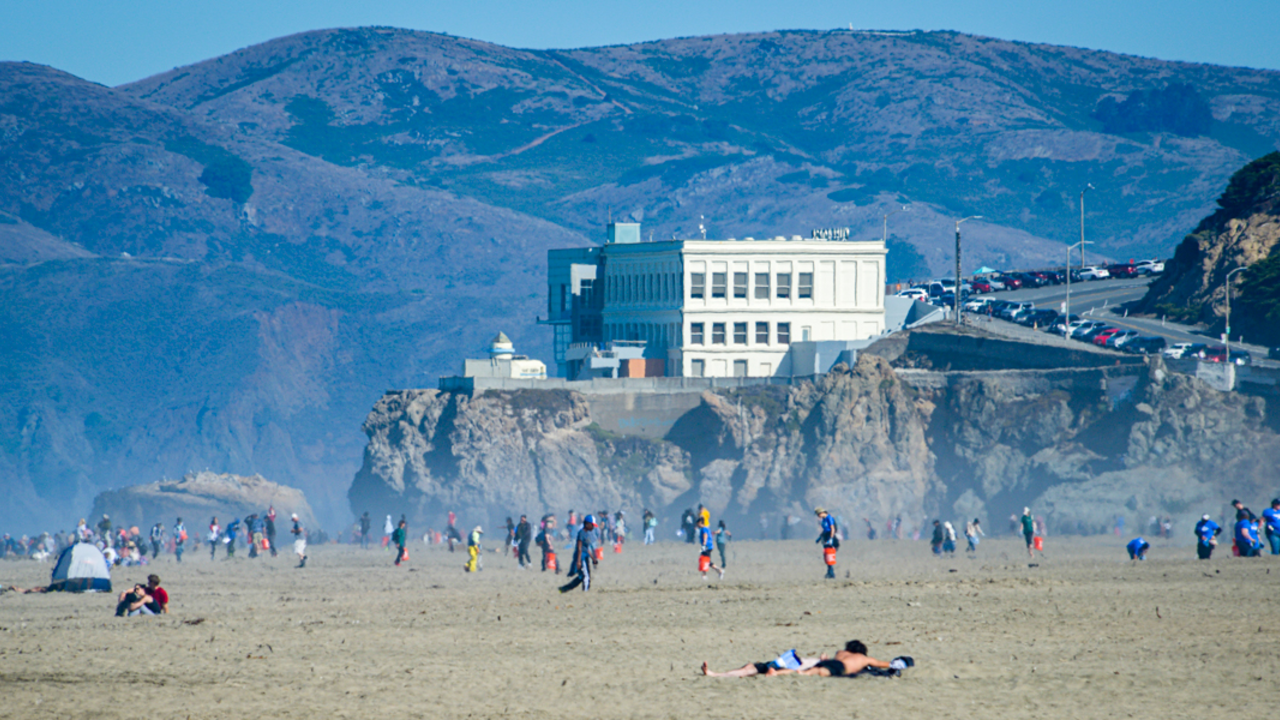 Park visitors and stewardship volunteers for Coastal Cleanup day mingle about on a busy day as the Cliff House restaurant looks over Ocean Beach.