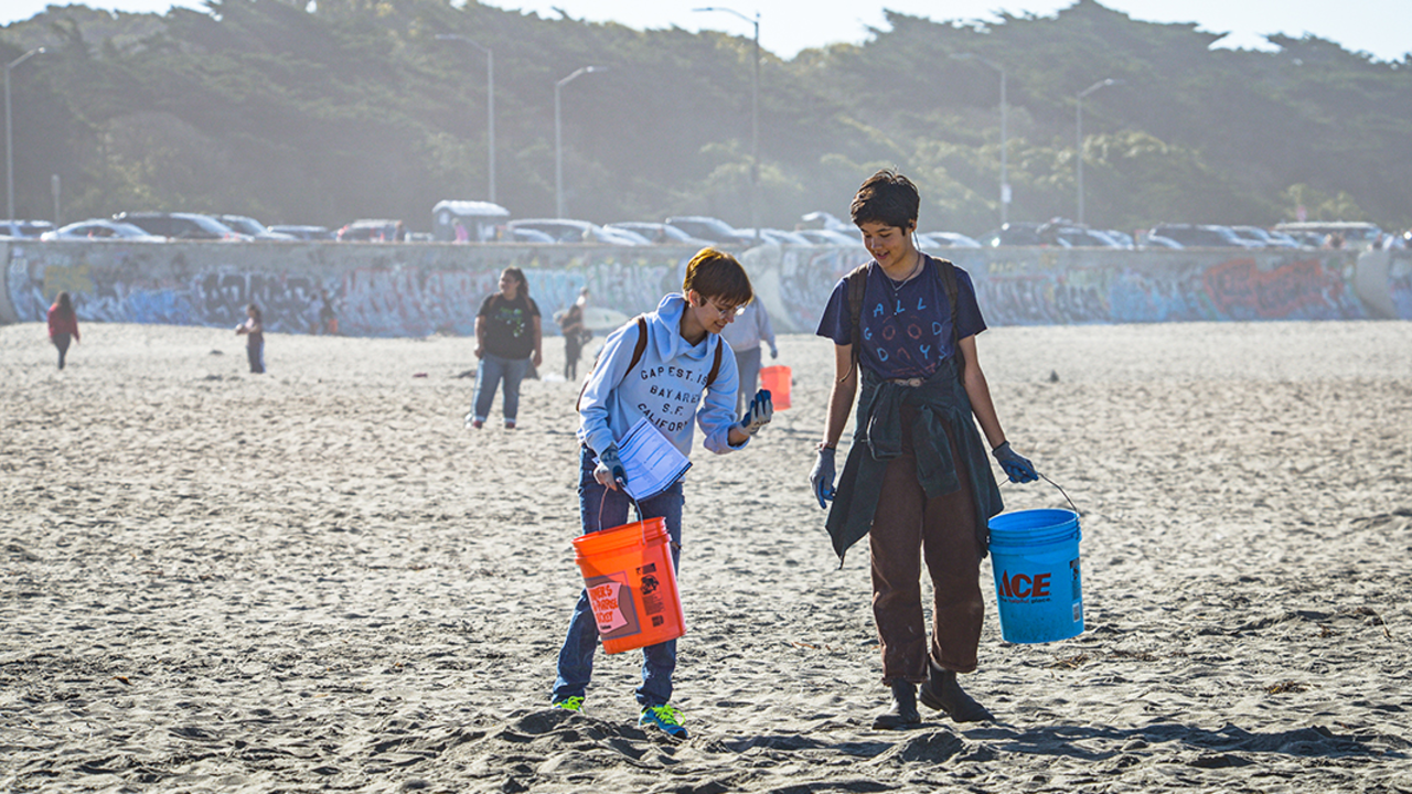Two volunteers on trash pick up walk down Ocean Beach with buckets. 