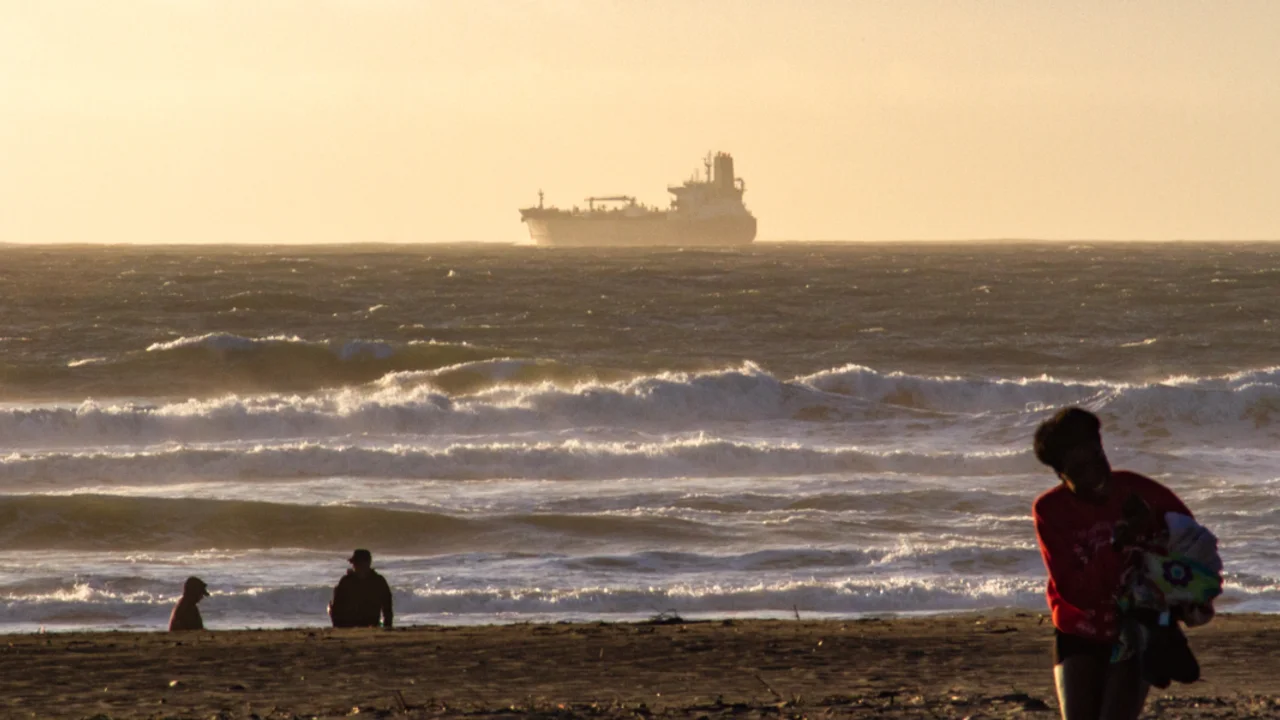 A large ship floats over the waves, along the horizon of Ocean Beach as park visitors enjoy the view of a sunset.