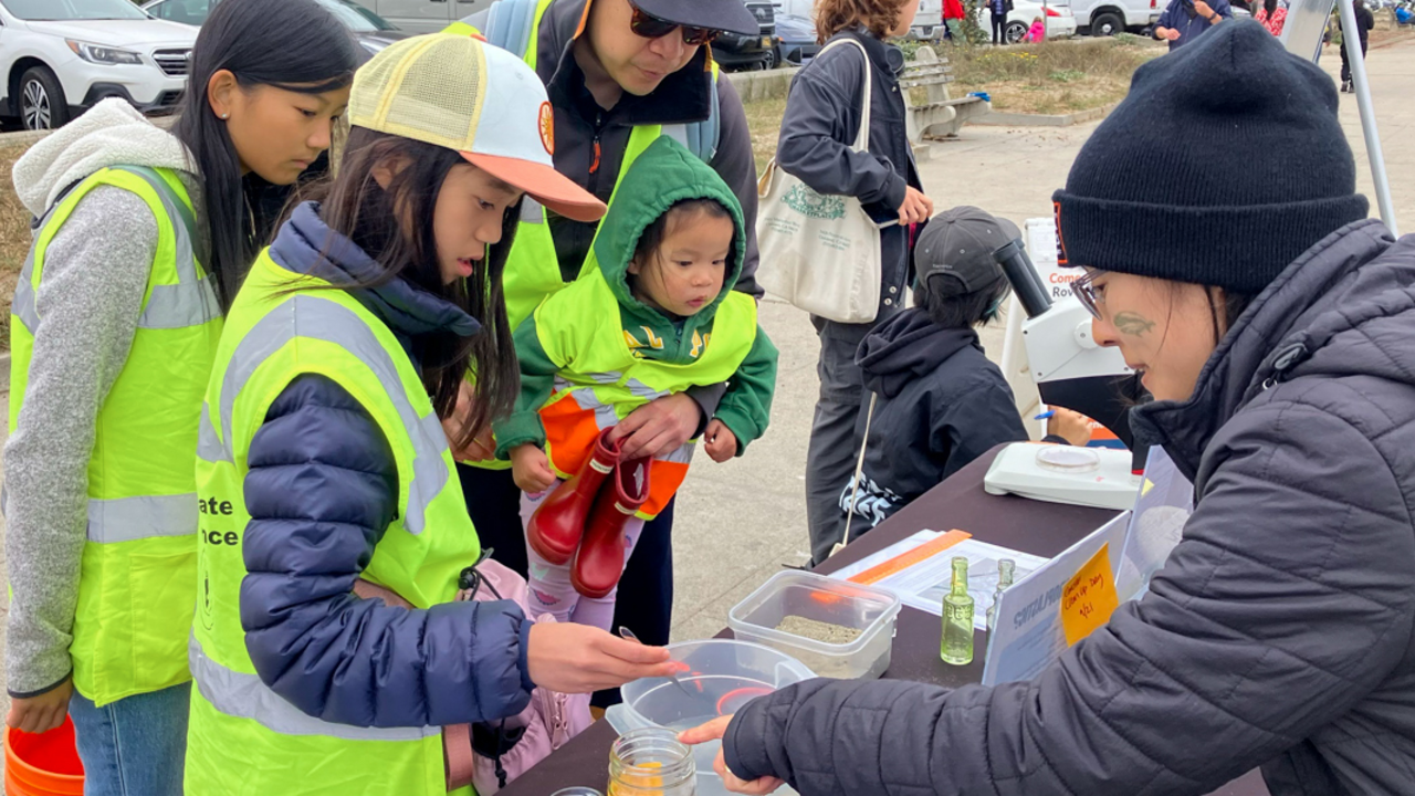 A family of beach cleanup volunteers stop by a table to learn about environmentalism