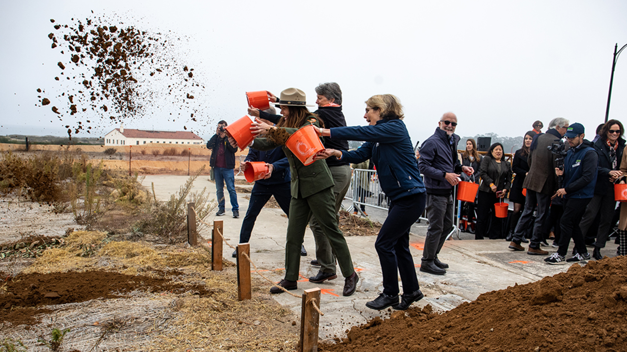 Three people throw buckets of dirt in the Presidio.