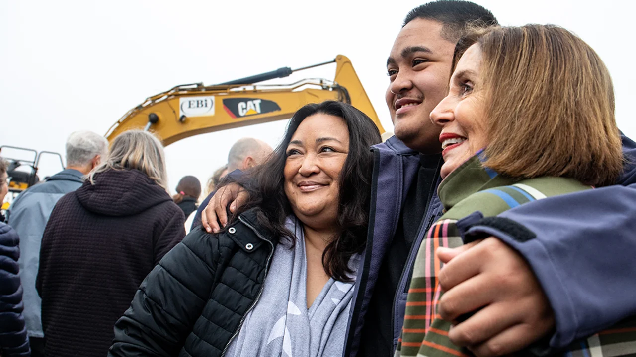 Three people embrace in front of excavator.