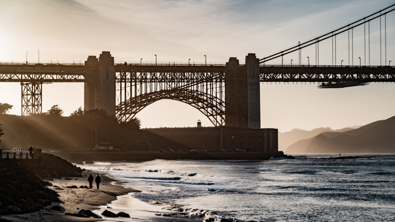 Sunlight filters through the silhouetted Fort Point and Golden Gate Bridge