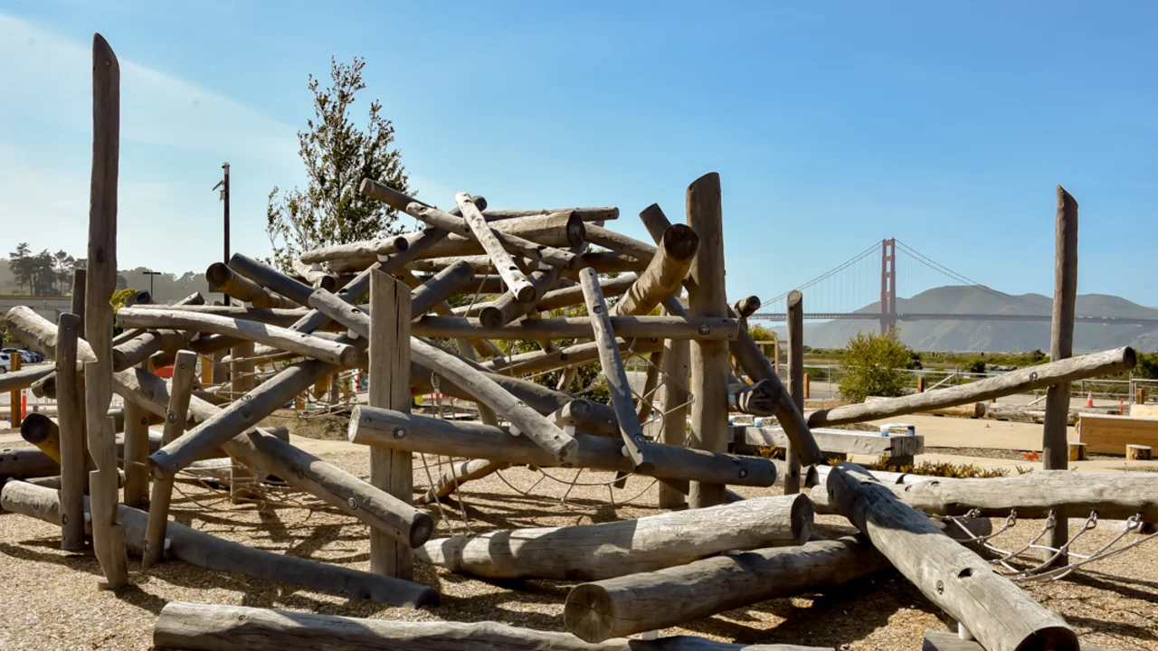 A playground structure made of wood logs at the Presidio Tunnel Tops Outpost, the Golden Gate Bridge is seen in the background.