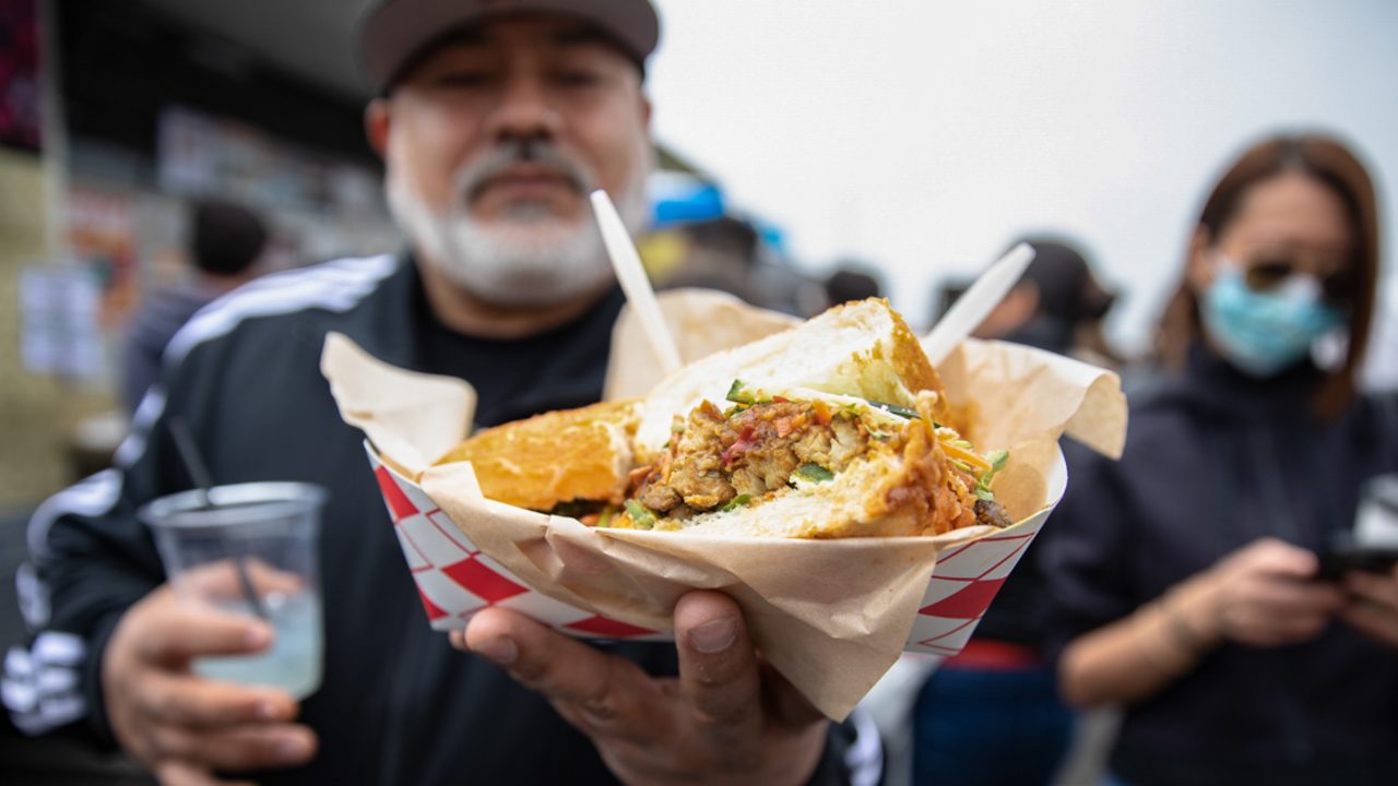 Visitors gathered around local gourmet food vendors for seriously good eats. A Tunnel Tops visitor holds out a delicious gourmet sandwich from the food vendors at Presidio Tunnel Tops.