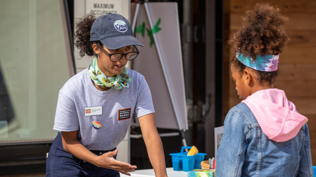 Parks Conservancy staff connecting with youth. Parks Conservancy staff member talking with a young girl at a Presidio Tunnel Tops event.
