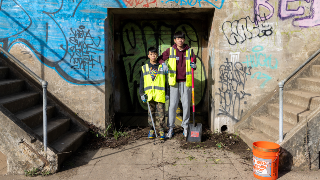 Two youthful volunteers in bright vests standing before the concrete wall at the Presidio Golden Gate Overlook battery