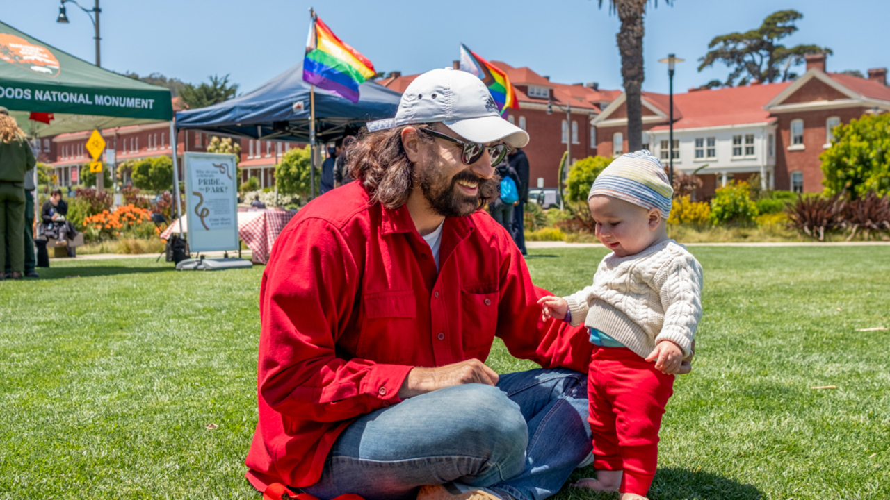 A father and child sit on the Presidio lawn during Pride at the Presidio event.