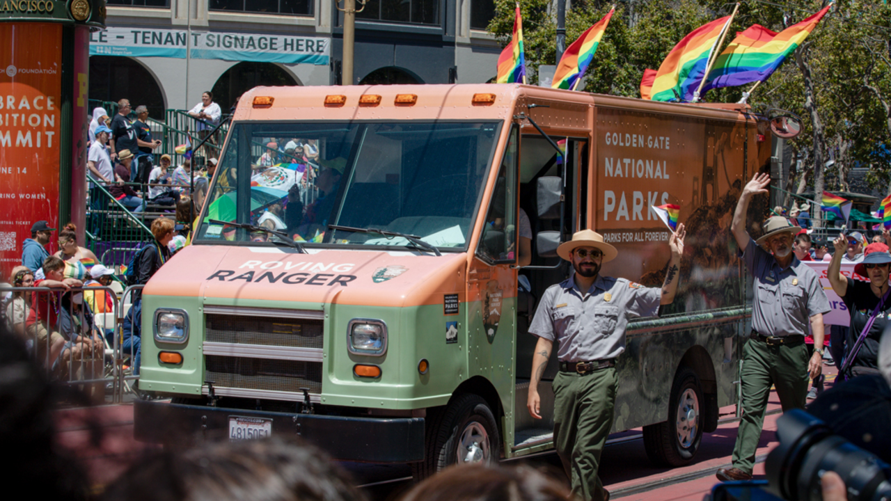 NPS park ranger marches alongside the Roving Ranger mobile trailhead at the 2022 SF Pride parade.