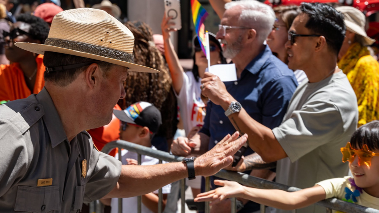 A ranger high fives a child wearing orange star sunglasses at the 2024 SF Pride Parade.