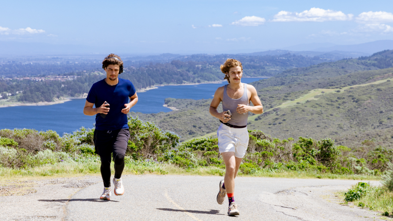 Sweeney Ridge Exercise Two runners exercise on a paved trail at Sweeney Ridge, with a beautiful sunny backdrop of san andreas lake.