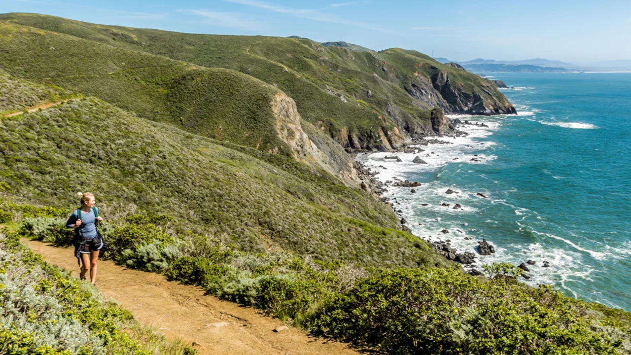 A hiker looks out at scenic view of the pacific coastline from the Coastal Trail in Marin Headlands on a bright sunny day.