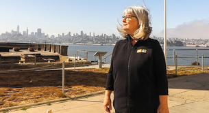 Nicki Phelps stands on Alcatraz Island with a view of San Francisco behind her.