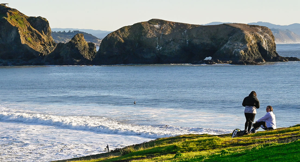 People on a green bluff overlooking the waves of the Pacific Ocean.