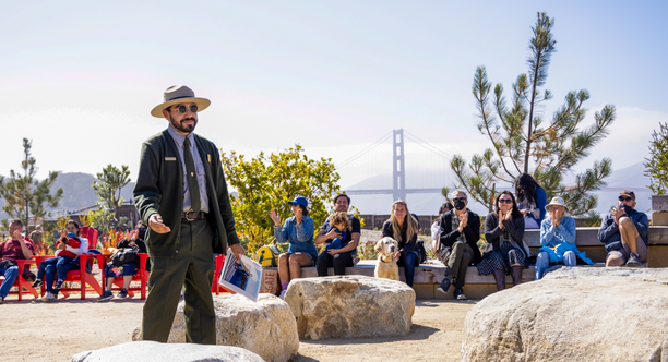 An NPS park ranger speaks to a seated crowd around the Presidio Tunnel Tops Campfire Circle